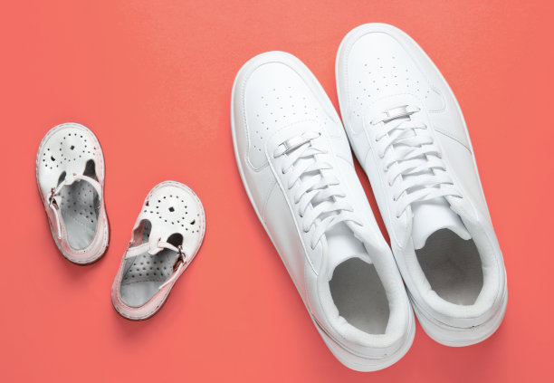 父亲节的概念。成人白色运动鞋和儿童凉鞋在粉红色的背景。图片下载