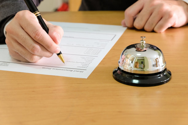 男人在酒店前台填写预订单，呼叫铃提醒提供服务。酒店服务概念图片下载