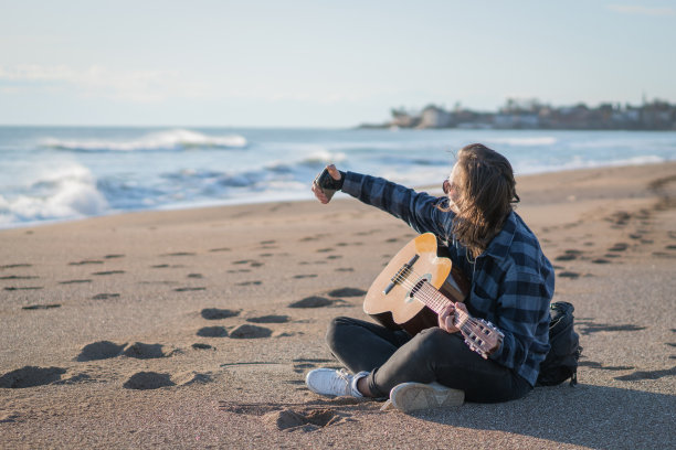 帅哥一边弹古典吉他一边在沙滩上自拍。图片下载