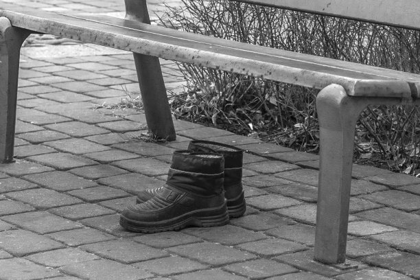 冬天的暖鞋留在公园的长椅下给无家可归的人。黑白照片。图片下载