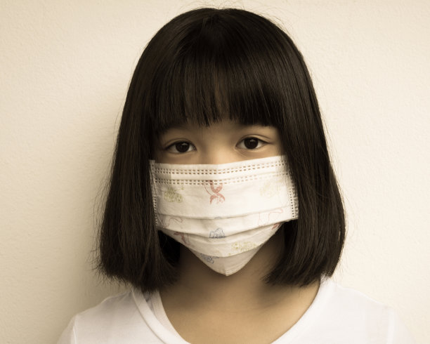 亚洲生病的女孩用口罩为孩子保护流感。一个可爱的小孩患有呼吸道疾病或流感的特写照片。可爱的小生病的女孩，带着医用口罩，复古的深褐色调。图片下载