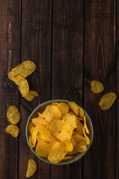 俯视图绿色盘子上美味的波纹金黄薯片油炸和盐在棕色的木头背景，快餐的概念图片下载