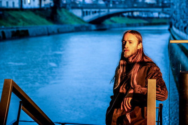 肖像沉思的人在橙色灯光下站在楼梯上反对蓝色的河流-股票照片图片下载