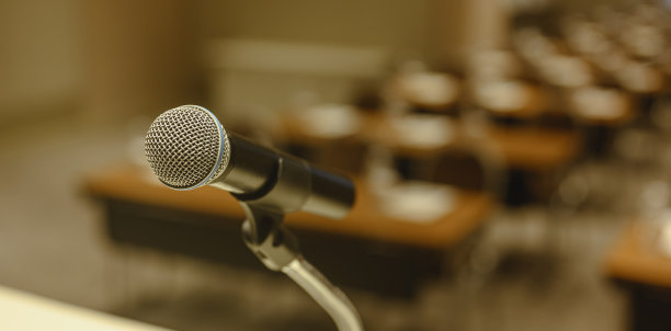 对会议室舞台上的麦克风进行特写。模糊的背景。麦克风，舞台，房间，班级，会议，问候概念。图片下载