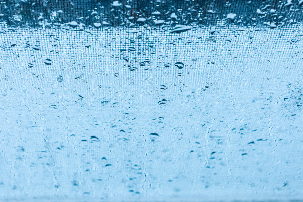 蓝色窗玻璃上的雨滴与模糊的溪流和网格抽象的背景。图片下载