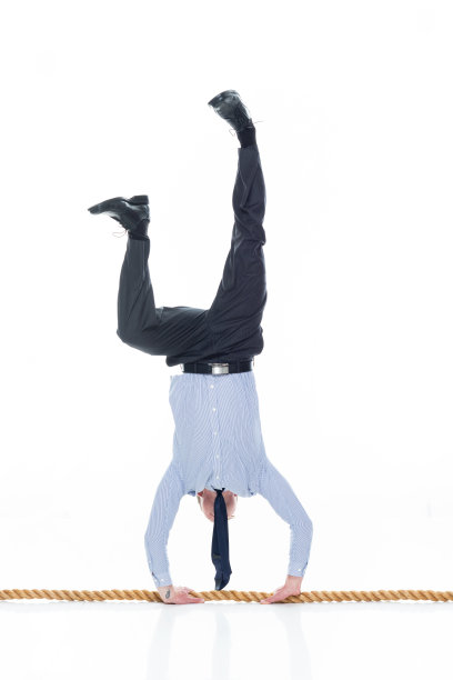 白人男性商务人员双手倒立在白色背景前，系着领带，积极进行运动训练，使用绳索图片下载