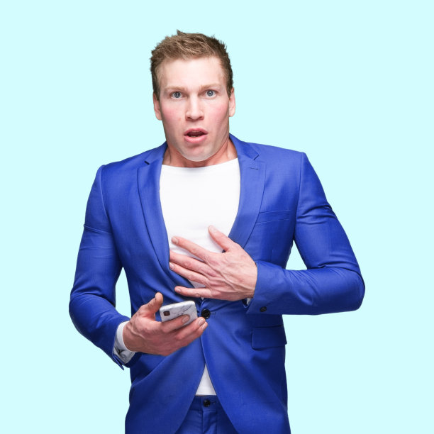 白人男性站在蓝色背景前，穿着智能便服，使用手机图片下载