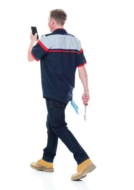 白人年轻男性修理工穿着制服，手持扳手，使用手机走在白色背景下图片下载