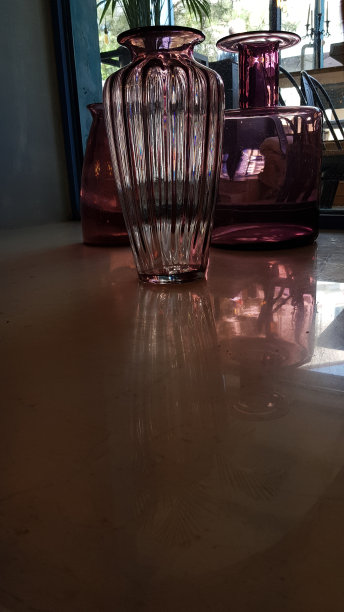 散焦静物与三个不同寻常形状的紫色花瓶在模糊的背景。透明的粉红色玻璃物体在室内与复制空间。图片下载