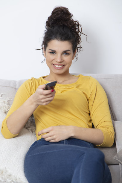 快乐的年轻女子一边用遥控器换频道一边看电视图片下载