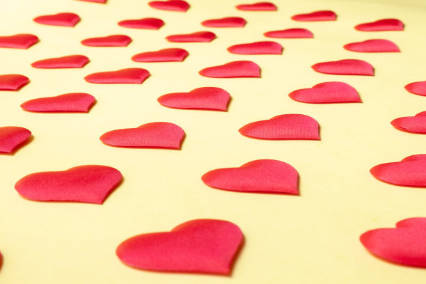 许多一模一样的红丝心交错地躺在黄色的背景上。象征着爱、温柔和激情图片下载