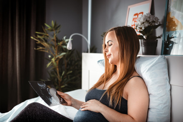 孕妇坐在床上看宝宝的超声照片图片下载