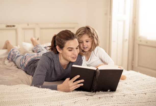 年轻的妈妈和可爱的小女儿一起读书。快乐的妈妈和可爱的金发女孩在床上阅读童话故事的生活方式形象。在幸福家庭中，育儿教育理念。图片下载