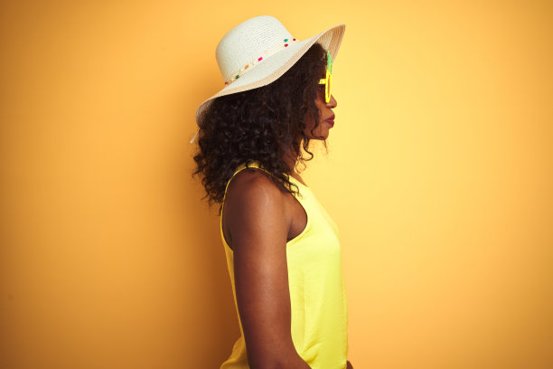 非洲裔美国妇女戴有趣的菠萝太阳镜在孤立的黄色背景看向一边，放松的侧面姿势与自然的脸自信的微笑。图片下载