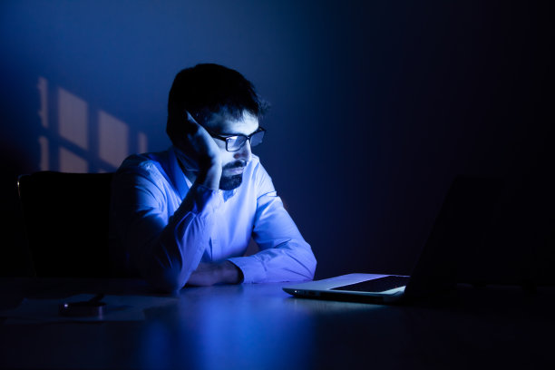 在黑暗房间里用电脑工作的悲伤男人图片下载