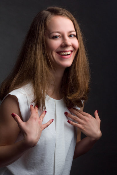 棕色头发，黑色背景，白色衬衫的女孩。他高兴地笑了。图片下载