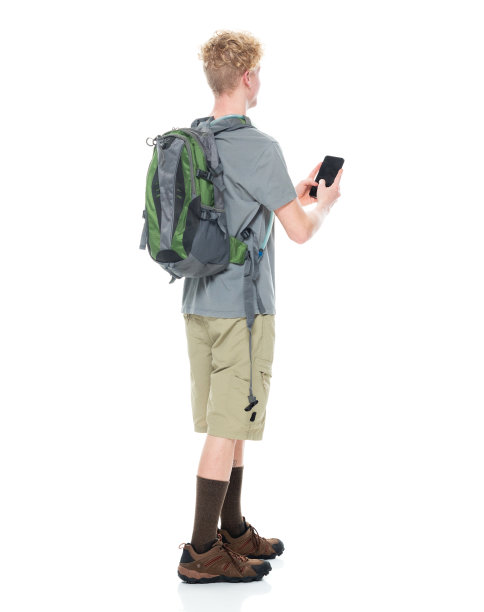 白人年轻男性背包客穿着登山靴，拿着包，用智能手机在白色背景前徒步旅行图片下载