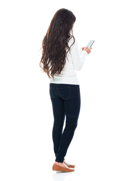 拉丁美洲和西班牙裔的年轻女性穿着牛仔裤站在白色背景前使用手机图片下载