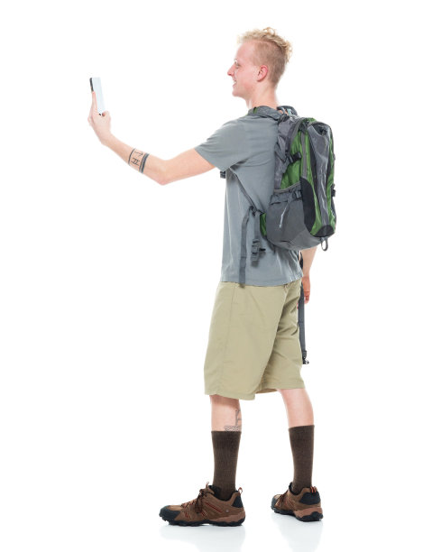白人男性徒步行走在白色背景下，背着背包，拿着包，使用手机图片下载