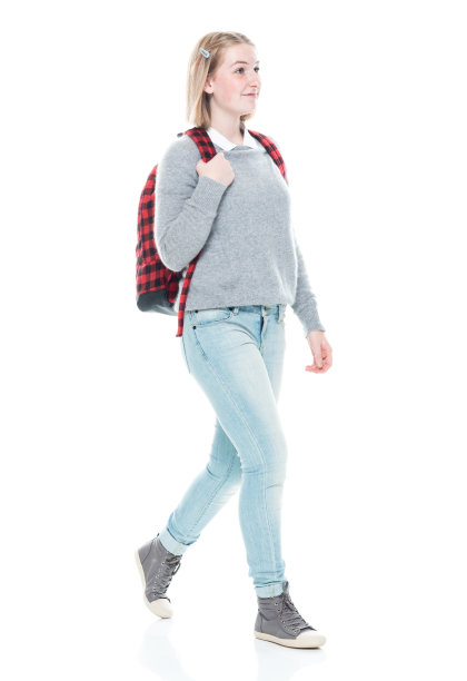z一代年轻的女高中生穿着牛仔裤拿着包走在白色背景前图片下载