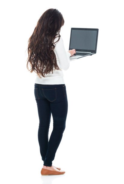 拉丁美洲和西班牙裔的年轻女性穿着牛仔裤站在白色背景前，使用笔记本电脑图片下载