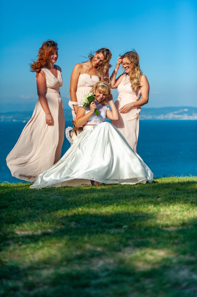 欢乐的新娘与伴娘坐在户外的肖像在多风的天气-股票照片图片下载