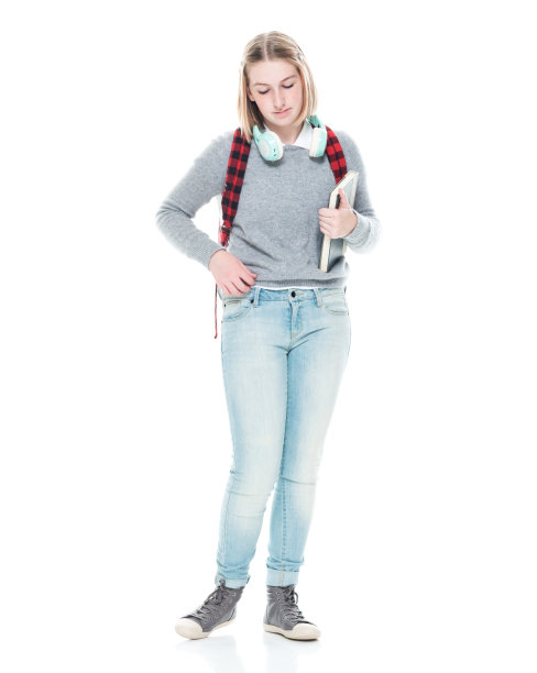 z一代的年轻女学生穿着牛仔裤站在白色背景前，拿着课本，戴着耳机图片下载