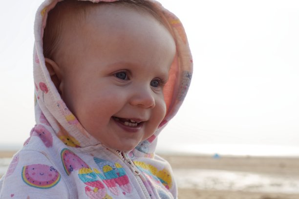 美丽的微笑可爱的婴儿，婴儿笑和戴兜帽，可爱的婴儿的特写肖像，温暖的滤镜，集中在脸上，美丽的表情可爱的快乐可爱的笑微笑的婴儿婴儿脸。图片下载