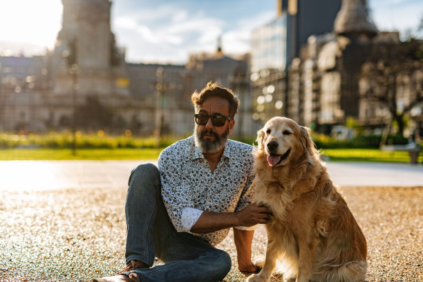 成熟的男人带着金毛猎犬在城市里散步素材图片