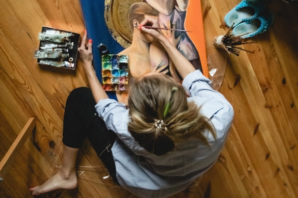 美丽的白人妇女在室内画图画。用画笔和颜料工作。温暖的室内氛围。周围柔和的光线图片下载