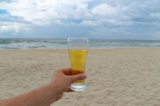 在阴天的沙滩上，男人们手拿着一杯啤酒图片下载