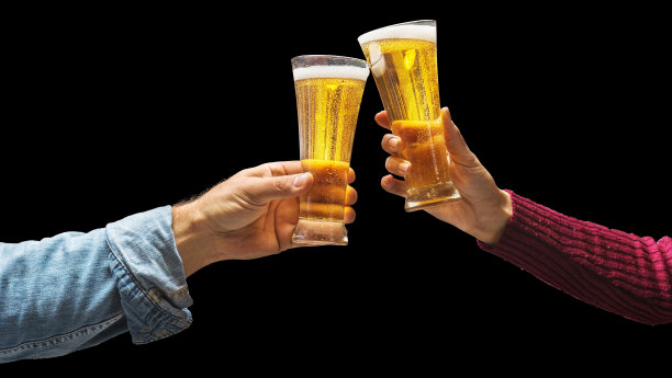 举啤酒杯庆祝。黑色背景上，男人和女人的手举起啤酒杯。文件包含剪切路径。图片下载