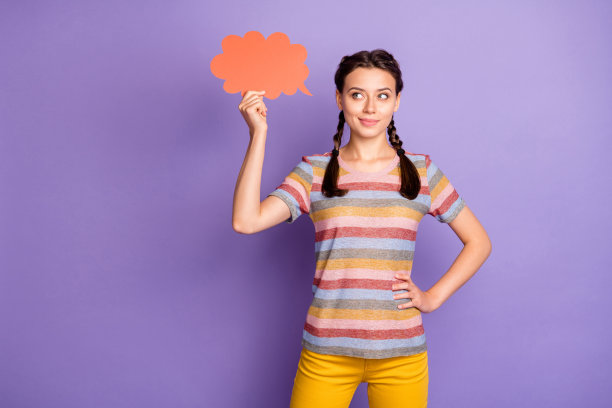 照片美丽的女士抱着大红色心云阅读横幅创意文字穿着休闲条纹t恤黄色裤子孤立的紫色背景图片下载