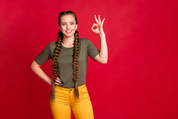 漂亮的青少年模特女士的照片显示ok符号表示同意好质量穿休闲t恤黄裤子孤立的红色背景图片下载