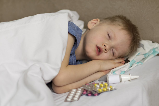 一个发烧头痛的小孩躺在床上。这孩子睡在毒品和药丸旁边。流感及感冒病毒图片下载