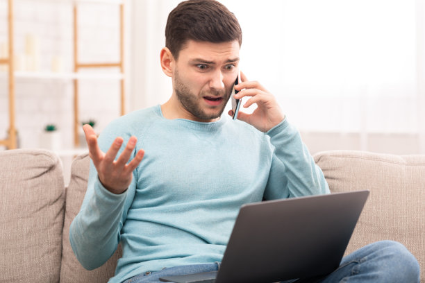不满的男人坐在室内用笔记本电脑致电客户支持图片下载