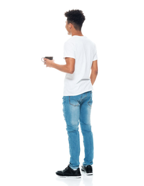 z一代的男孩穿着牛仔裤，拿着咖啡杯站在白色背景前图片下载