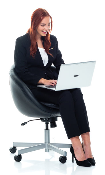 白人年轻女商人坐在白色背景前穿着商务装，使用笔记本电脑图片下载