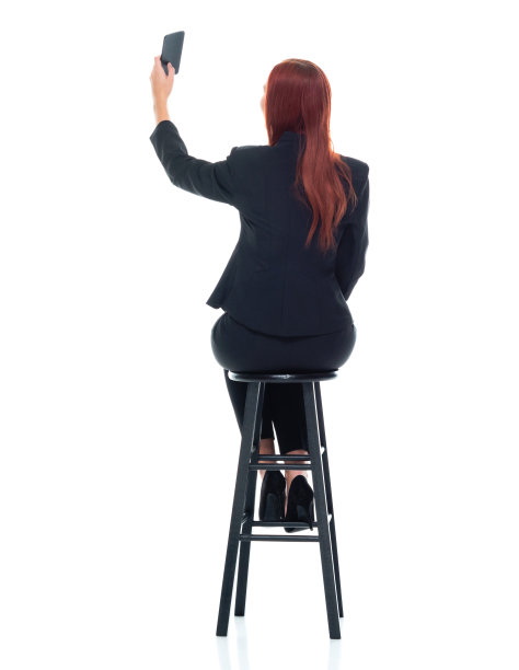 白人年轻女商人坐在白色背景前穿着商务装，使用手机图片下载