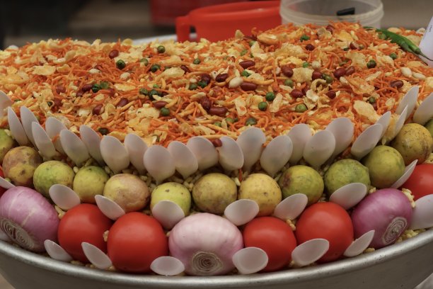 这是一个用绿豆芽、鹰嘴豆芽、烤花生、脆玉米片、印度辣小吃、印度当地市场上的健康食品，以西红柿、洋葱、柠檬作为调料图片下载