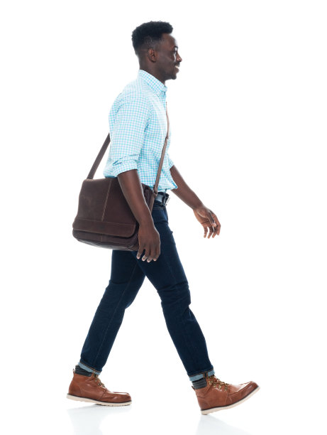 非裔美国男性穿着肩包和拿着包走在白人背景前图片下载