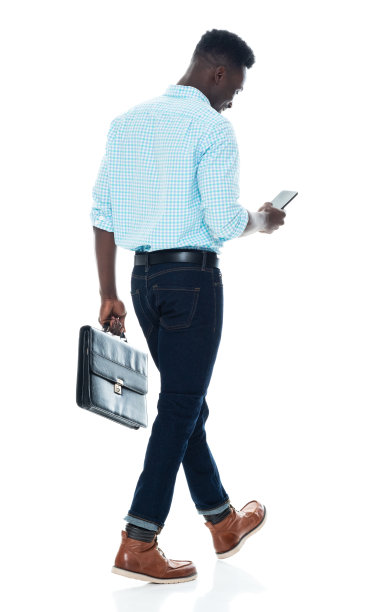 非洲裔男性穿着商务休闲装，手持公文包，使用手机走在白色背景前图片下载