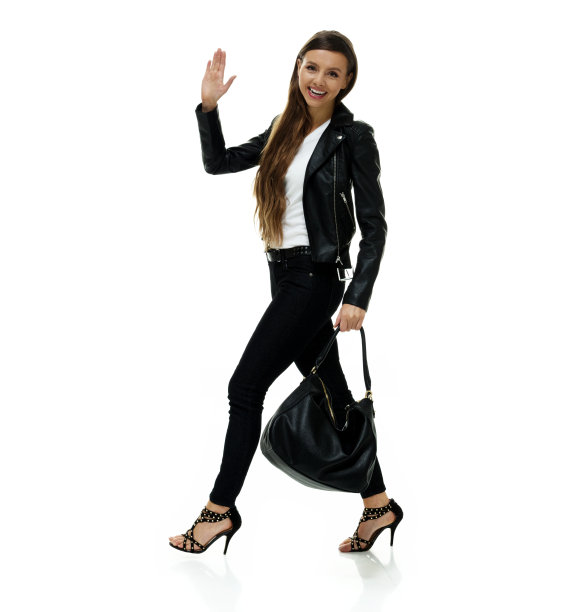 白种人年轻女性穿着皮夹克，拿着钱包走在白色背景前图片下载