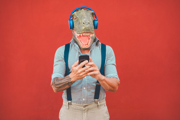带着t-rex面具的纹身男子一边听音乐一边用智能手机-疯狂的高级男子从手机应用程序中选择播放列表-科技趋势和疯狂的服装概念-专注于脸部图片下载