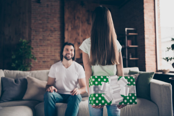 小女士的照片背后持有准备的生日大绿色礼盒英俊的爸爸坐在舒适的沙发深情微笑模糊焦点房子房间室内图片下载