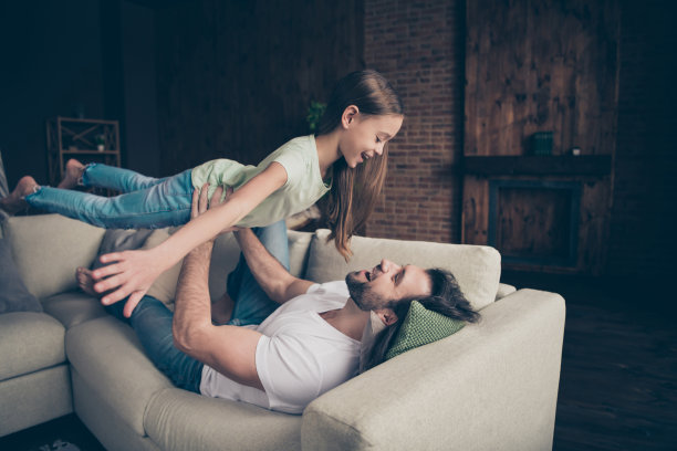 资料照片的小有趣的女士英俊的爸爸躺在舒适的沙发好心情拿着他的公主的手举起空气展开像翅膀的手假装飞行的房子房间在室内图片下载