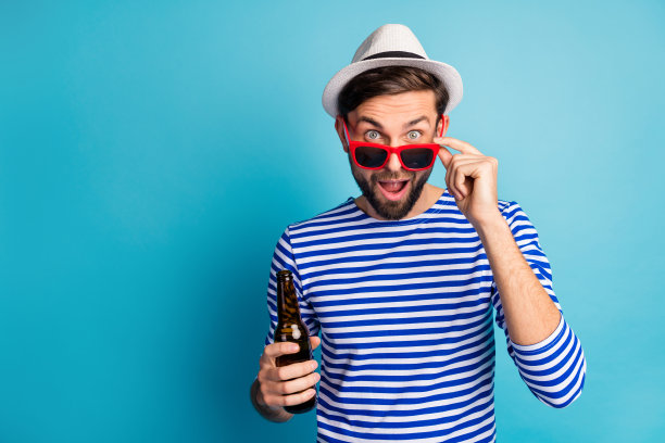 时髦的好旅行者的照片，家伙喝啤酒瓶子所有包括异国情调的度假胜地看到广告横幅，购物价格，戴太阳眼镜条纹水手衬衫帽孤立的蓝色背景图片下载