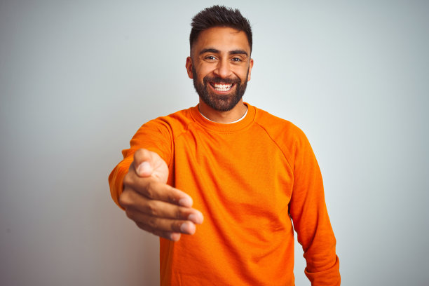 身穿橙色毛衣的年轻印度男子友好地握手图片下载