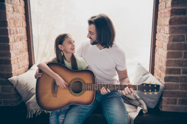 小可爱的漂亮女士和她帅气的年轻爸爸的照片坐在窗台上抱着木吉他教新和弦度过周末的时间房子房间在室内图片下载