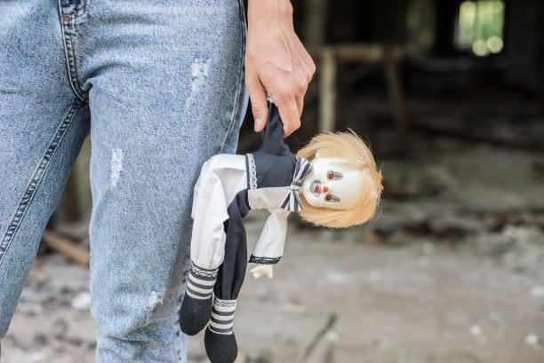 女孩手持小丑玩偶，背景是损毁的建筑，关于孤独、被遗弃儿童、家庭暴力的概念图片下载